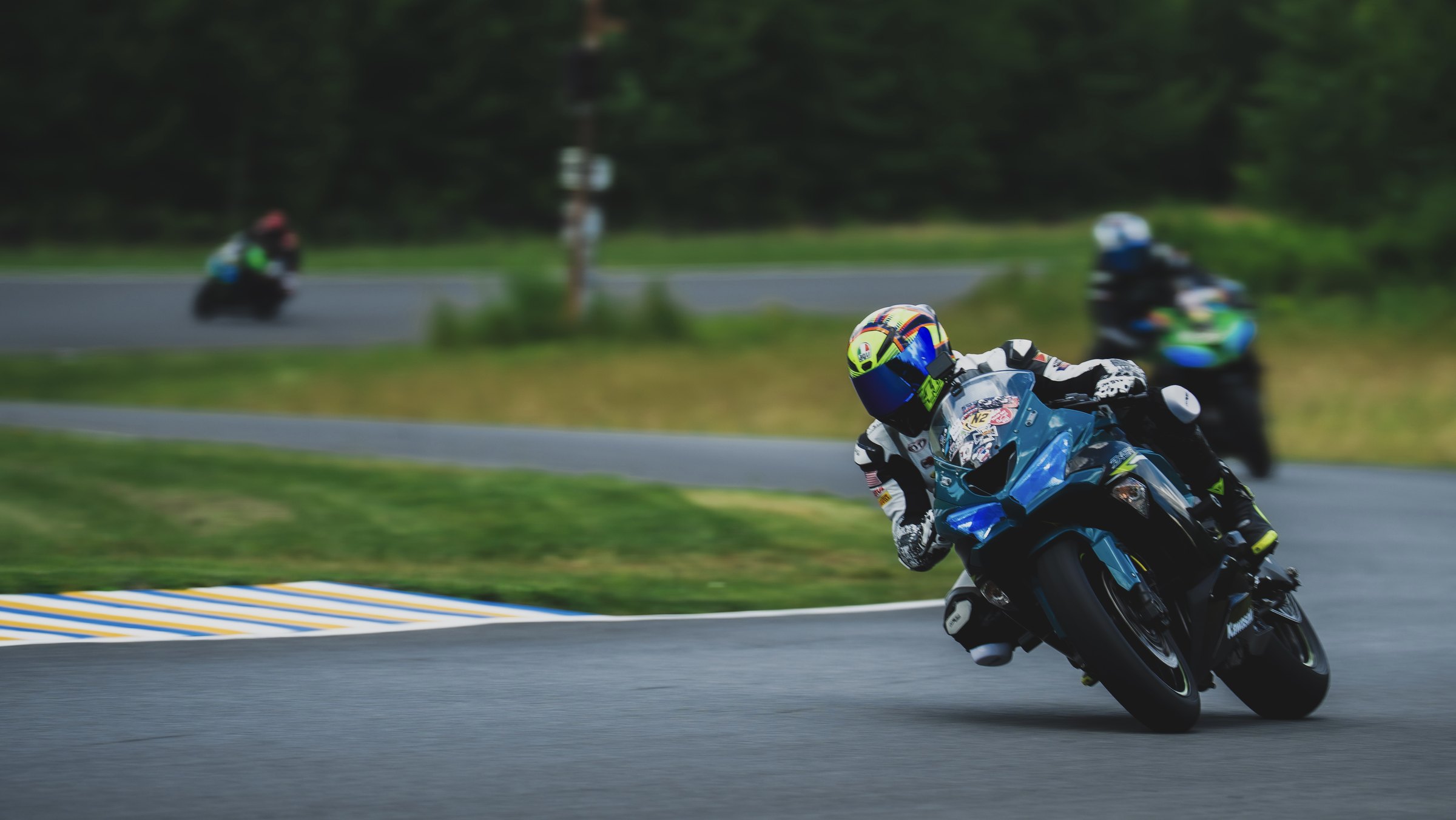 Rider on a blue Kawasaki leaning into a corner with two riders behind
